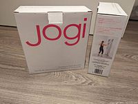 Boxes of two Jogi over-the-door resistance band systems, showing the brand and packaging with exercise demonstration picture