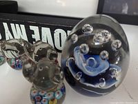 Front view showing 4 glass elephant paper weights with multicolored millefiori beads at base and a large blue flower paperweight with bubbles in clear glass.