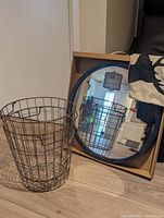 Two metal wire baskets and new round mirror reflecting the room, mirror in box.