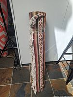 Rolled up Ikea replica wool Yenice kilim rug showing the fringe edge and woven geometric pattern in warm colors.