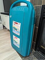 Rubbermaid rolling tote in teal and beige, with handle and wheels position view.