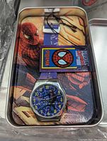Individual Spiderman watch in a tin gift box showing Spiderman themed analog watch with comic-style face and tag.