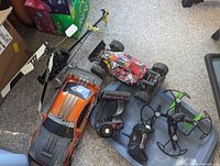 Full lot overview showing RC helicopter, two RC cars, drone, and two remote controllers on carpeted floor.