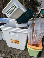 Stacked assortment of plastic storage bins including white and dark green baskets, clear plastic containers, and colored magazine holders in orange and lime green