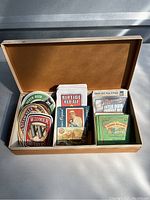 Open wooden box containing three compartments filled with assorted beer coasters from various breweries like Widmer Brothers, Riptide Red Ale, and Sierra Nevada Pale Ale.