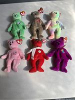Photo of six collectible Beanie Babies bears arranged in two rows on a white surface with tags still attached