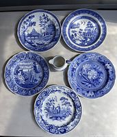 Top side view showing the five plates displayed around a small creamer, showcasing varied blue and white intricate transferware designs with floral and scenic motifs.