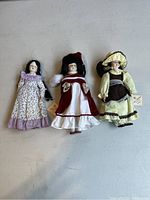 Three collectible country porcelain dolls in various dresses, two with tags attached and one without.