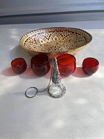 Photo of the red and gold decorative bowl, four red glass candle votives, and a pewter candle snuffer on a white surface.