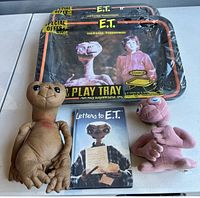Front display of lot items showing two E.T. plush dolls, two metal trays wrapped in plastic, and a book titled 'Letters to E.T.'