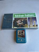 Photo of the Italian edition Scrabble game in shrink wrap and the vintage home baseball game tin placed beside it.