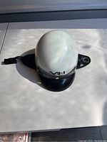 White vintage police helmet with black visor and chin strap, VR-1 branding front, minor scuffs visible.