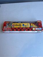 Photo showing unopened original box containing the 2002 M&Ms Racing Champions NASCAR transporter and diecast race car. The box shows wear and tear but the item inside is brand new.