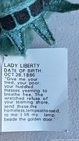 Close-up of the Lady Liberty bear's tag showing the date of birth Oct 28, 1886, and an excerpt of the poem associated with Lady Liberty.