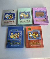 Five DVD boxed sets for The Simpsons first through fifth seasons with collector's edition artwork featuring Simpsons characters on TV screen on covers.