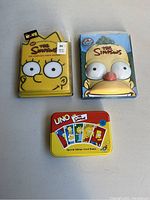 Lot with two Simpsons collectible DVD sets (Season 9 and 11) in metal character tins plus a special edition Simpsons UNO card game in a red metal tin.