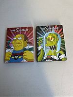 Two DVD box sets for The Simpsons, Season 12 and Season 14, on a light background showing front cover art.