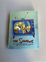 Photo of a hardcover DVD collector's edition case for The Simpsons complete second season showing the Simpsons family on a TV screen graphic.