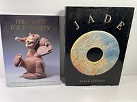 Two books standing side by side: one about jade with a black hardcover showing a jade bi disk, the other titled 'The Quest for Eternity' featuring a ceramic mythical creature sculpture on the cover.