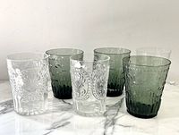 Photo of 6 pressed glass highball glasses on marble surface, 3 clear and 3 green/blue tint, showing embossed decorative patterns.