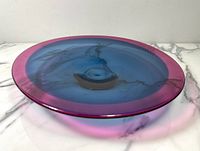 Side angle view showing round dish with blue and pink-purple color tones and a glossy finish.