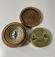 Compass set in round wooden box with brass details, showing compass face and open lid alongside gold-toned calendar.