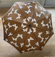 Top view of the open umbrella showing the brown fabric with white butterfly pattern and white trim edge.