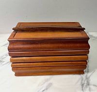 Front view of cherry and walnut wood box closed with the lid on showing carved tiered edges and walnut wood accent handle on lid.