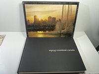 Top-down view of the book open to the title page 'expo 67 montreal canada' showing black hardcover with white text.