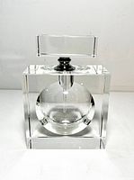 Front view of clear geometric glass perfume bottle with circular hollow center and rectangular stopper on white background
