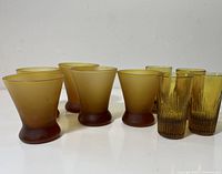 Group of nine mid-century modern amber liqueur glasses, 5 frosted and 4 clear textured, arranged on white surface.