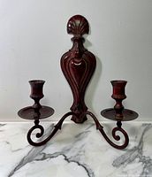 Front view of metal wall sconce candle holder showing deep oxblood red patina and decorative backplate with two candle holders on scrolling arms.