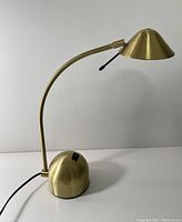 Front view of gold toned desk lamp with curved arm and conical shade showing overall shape and condition.