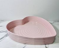 Pink heart-shaped ceramic bowl with ridged sides and concentric circular design inside, placed on marble surface.
