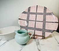 Photo showing jug, oval baker, and vintage cake plate with pink and black grid pattern on marble surface.