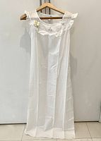 Full view of the vintage white cotton nightgown hanging on a wooden hanger showing overall length and style