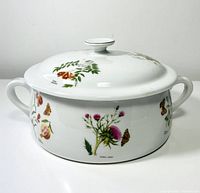 Front angle of white porcelain casserole with floral and butterfly illustrations, showing overall design and shape with handles and lid knob.