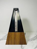 Front view of Vitnner metronome showing wood-patterned base and black pyramid top, missing front cover.