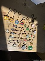 Assorted vintage keychains featuring various logos and designs laid out on a wooden surface.