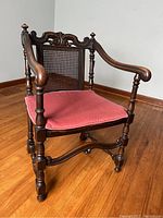 Front angle showing full chair, cane back, seat with cushion, carved wood frame, armrests, and turned front legs.