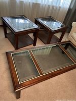 Set of three tables including one large coffee table and two smaller matching lamp tables, featuring dark wood and smoked glass insets.