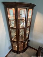 Front view of the corner china cabinet showing glass panes, multi shelves, and lighting inside.