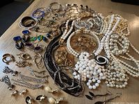 Photo showing multiple necklaces and earrings including pearl strands, metal chains, and various clip-on and dangling earrings spread out.