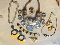 Overview of assorted costume jewelry items including necklaces, brooches, earrings, and bracelets displayed on light wood surface