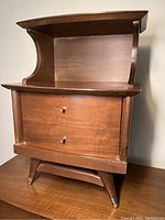 Clear frontal and angled views of mid century Krug bedside table showing wood grain, drawer knobs, and dovetail drawer construction with Krug stamp.