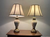 Pair of table lamps with brass bases and ceramic bodies topped with fabric shades on a wooden surface.