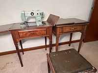 Two wooden sewing tables side by side, one with vintage green sewing machine, one stool in front