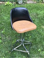 Full view of vintage swivel stool showing black vinyl backrest, tan vinyl seat, and chrome legs on grass background.