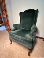 Front angle view of the green velvet wing back chair showing upholstery details and wooden cabriole legs.