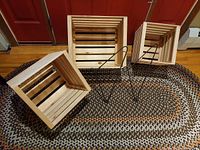 Three nesting wooden crates displayed on a braided rug, with two wrought iron hangers placed alongside.